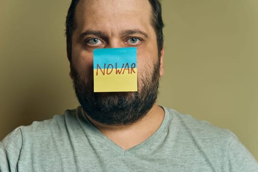 A bearded European man with a sticker attached to the nose, in the form of a Ukrainian flag with the inscription no war