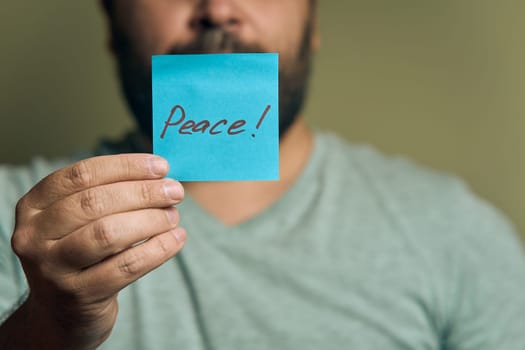 A bearded European man holds a blue sticker in front of him, with the word peace