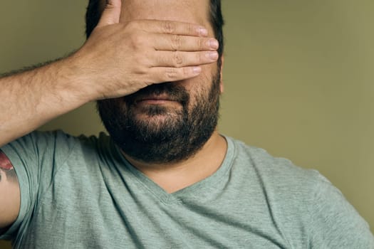 A bearded European man covers his eyes with his hand