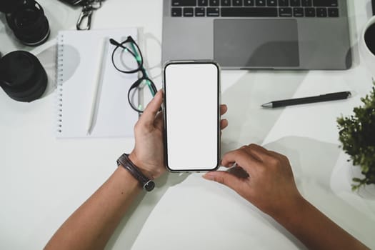 Overhead view of woman holding smart phone over white office desk. Blank screen for your advertising text message.