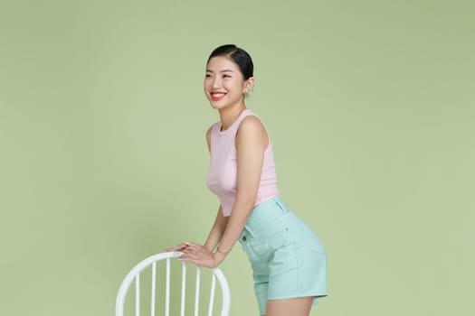 Asian woman standing near chair on green background