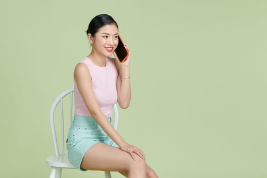 Pretty smiling girl talking on the smartphone and sitting on the chair