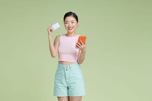 Portrait of a happy young girl showing plastic credit card while holding mobile phone