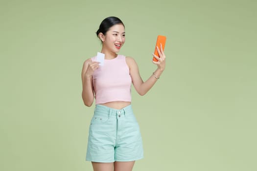 Pleased young woman using mobile phone holding debit card.
