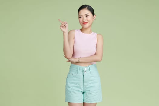 Young elegant woman pointing at plastic green background