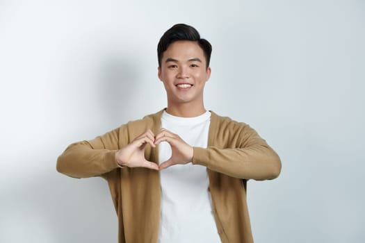 Smiling asian man makes heart gesture demonstrates love sign expresses good feelings and sympathy.