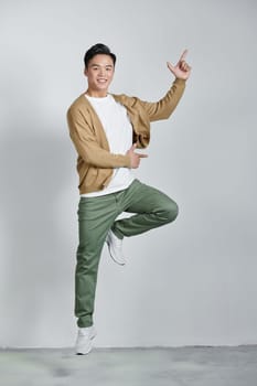excited young Asian man jumping and pointing hand to empty space aside studio shot