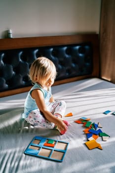 Little girl sitting on the bed in front of the puzzle pieces. High quality photo