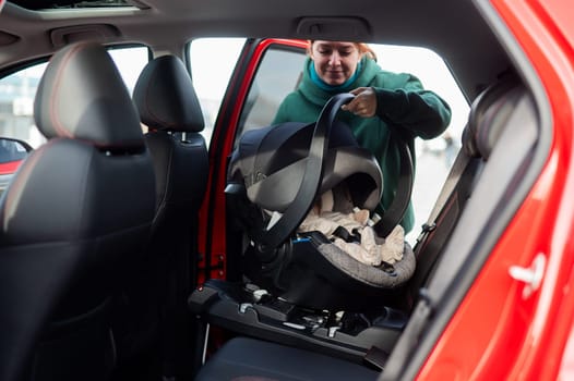 A Caucasian woman puts a child seat with a newborn baby in the car. Quick fastener