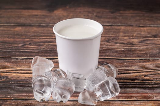 Cold milk in cardboard takeaway glass on wooden table