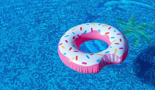 A rubber bitten donut with caramel sprinkles floats in the clear blue water of the pool.