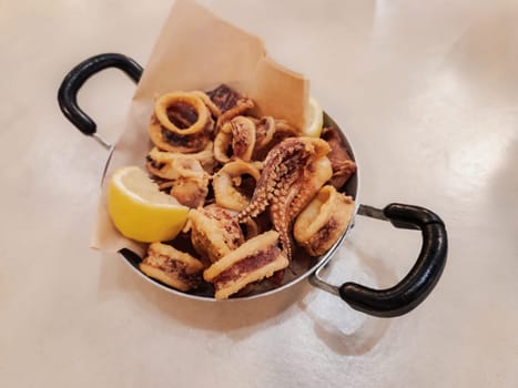 Fried squid slices served on iron cast pan with a slice of lemon. Crisply calamari tavern food concept.