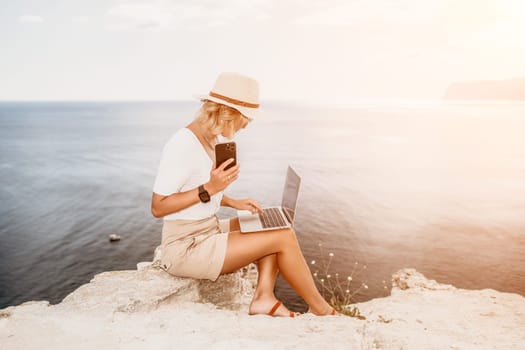 Digital nomad, Business woman working on laptop by the sea. Pretty lady typing on computer by the sea at sunset, makes a business transaction online from a distance. Freelance remote work on vacation