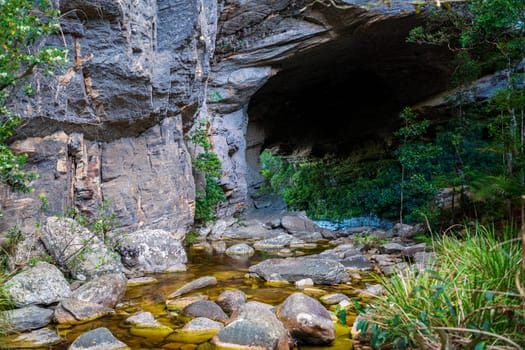 A tranquil cave by a forest with a serene stream.