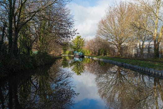 View from a narrowboat travelling in English rural countryside scenery on British waterway canal with moored boat