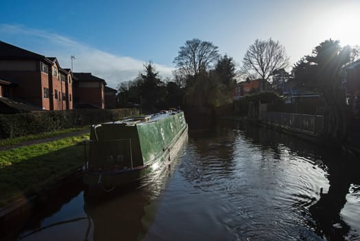 View from a narrowboat travelling in English urban village scenery on British waterway canal with moored boat