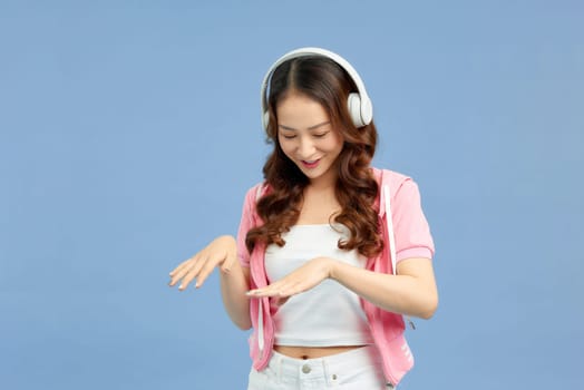 Young asian woman wearing headphones dancing active over blue background