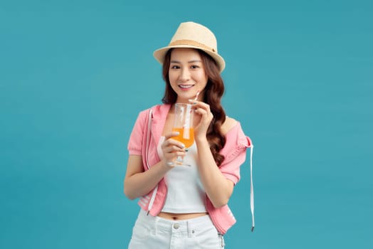 Beautiful smiling Asian woman with a glass of orange juice isolated on colorful blue background