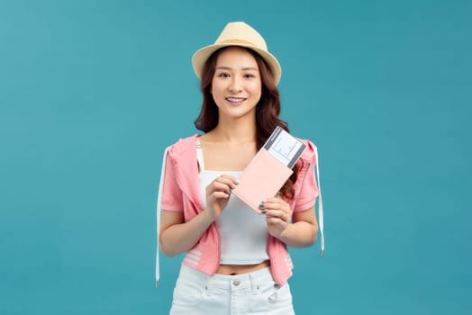 Happy Asian woman traveler with passport and boarding pass ticket isolated on blue background