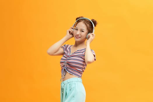 Young satisfied fun woman wear headphones listen to music isolated on yellow background
