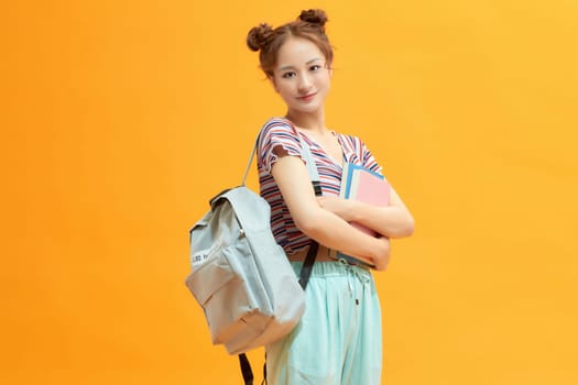 Young happy student with backpack on yellow background