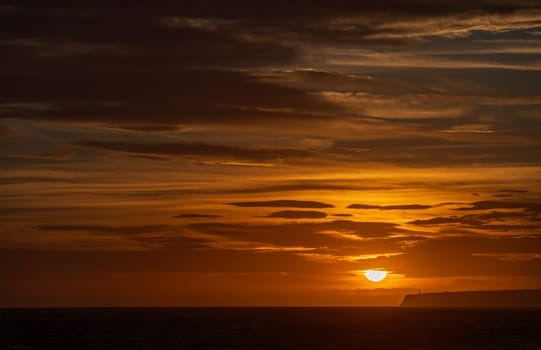 Lighthouse on cliffs with a sunset, orange clouds, and dark sea horizon.