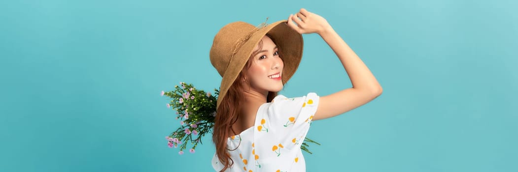 A beautiful young woman in summer dress and straw hat holding wildflowers bouquet