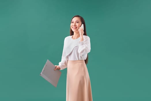 Businesslike happy woman holding clipboard with files in office and calling with mobile phone 