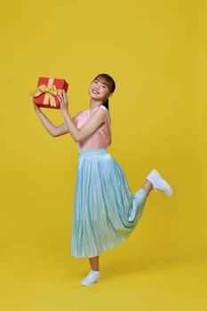 Happy pretty young woman jumping and holding wrapped gift box smiling isolated on yellow background