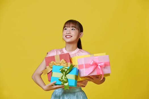 Smiling. Portrait of stylish woman emotionally posing with present boxes over yellow background