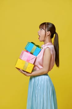 A smiling pretty girl holding stack of gift boxes isolated over yellow background