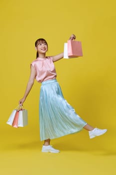 beautiful girl in elegant spring dress holding shopping bags on yellow background