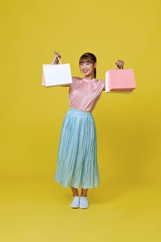 Pretty Asian woman carrying colorful shopping bags in purple color studio background