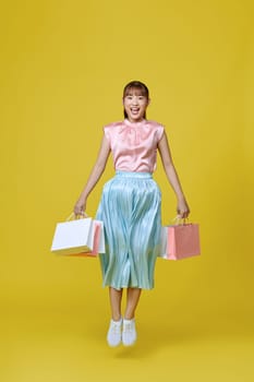 Full length profile of cute millennial lady run with bags isolated on yellow background