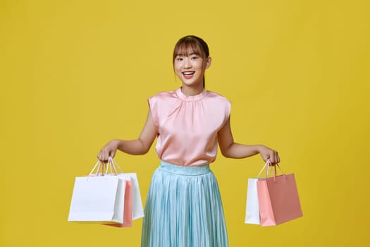 beautiful girl in elegant spring dress holding shopping bags on yellow background