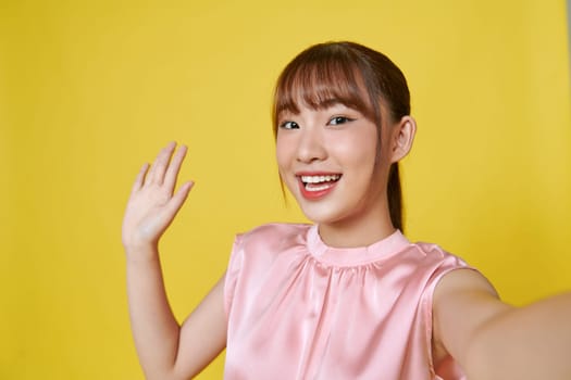 Dreamy cute young lady recording self video showing arm empty space isolated on yellow background