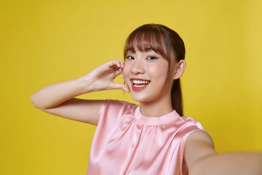 Young woman standing isolated on yellow background taking selfie photo winking to camera posing smiling playful