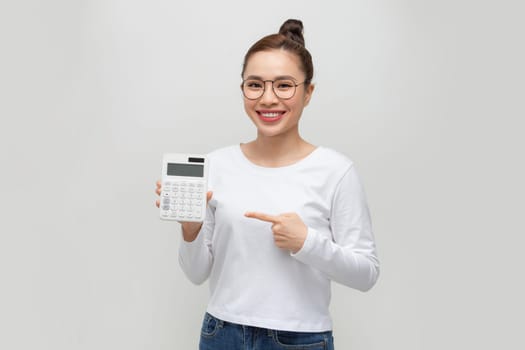 Pretty young businesswoman pointing at calculator on white background