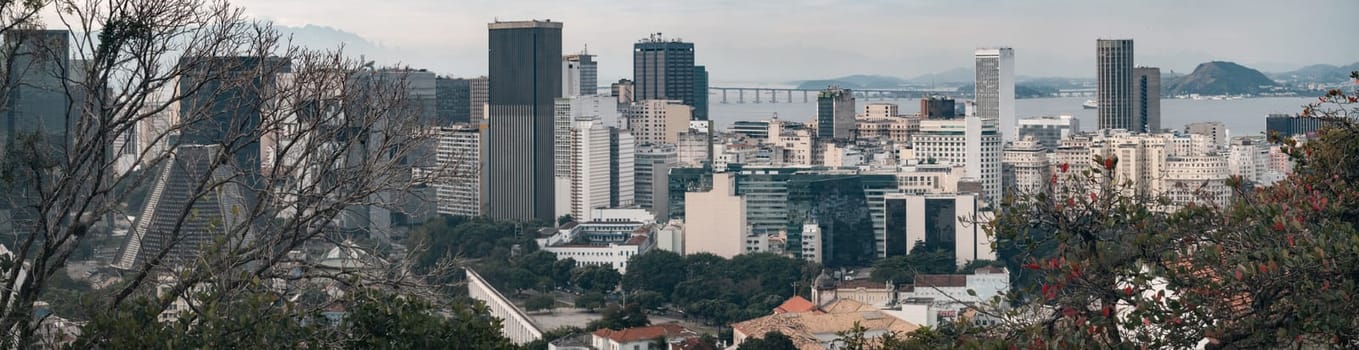 Cityscape displays tightly-packed buildings with a bridge over the sea in the distance.