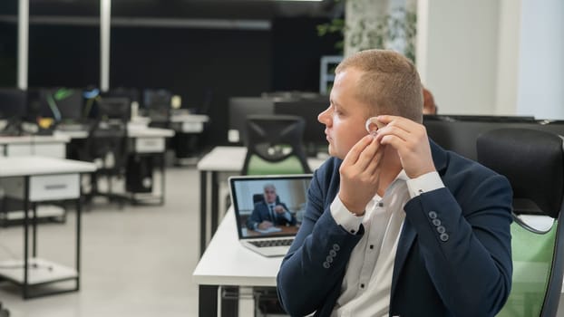 Caucasian man putting on hearing aid to online meeting on laptop