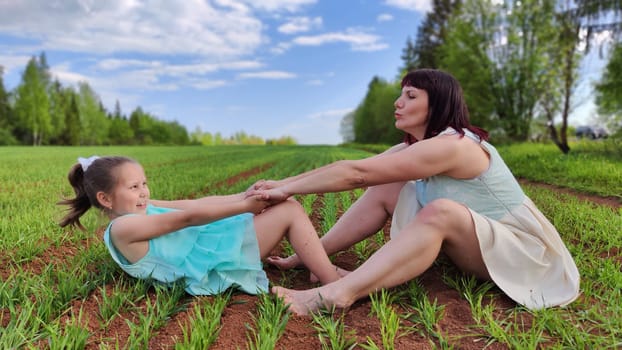 Happy mother and daughter enjoying rest, playing and fun on nature in green field. Woman and girl resting outdoors in summer or spring day