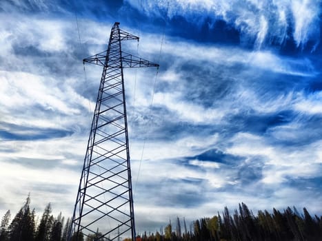 Power lines on a hill, hill or in the mountains against a blue sky with white clouds. Electric lines, towers, wires in nature landscape