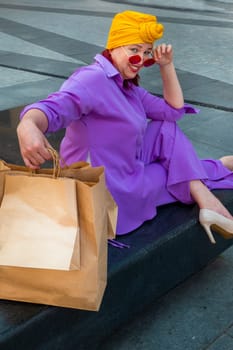 woman with craft shopping bags in the city. The concept of fashionable Consumerism and ecology. An adult Asian woman in a purple suit with red and yellow accents enjoys shopping . a sunny day.