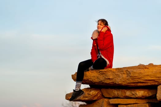 Beautiful Caucasian woman sit on the rock near cliff on the mountain and action of feeling cold and look forward with warm light in the morning.