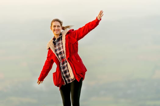 Beautiful woman stand near cliff with background of grass field and rural village area in view on the mountain with warm light of sun rise and she look happiness with smiling.