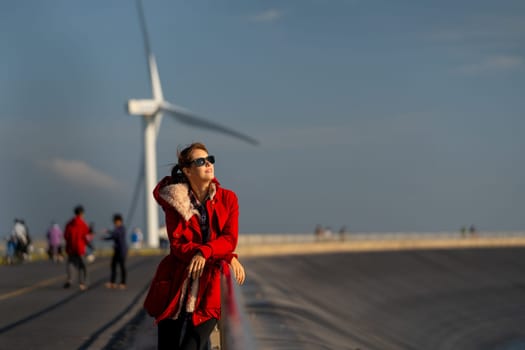 Close up beautiful Caucasian waman with sunglasses stand in front of wind turbine or windmill near the road with smiling of happiness.