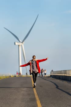 Caucasian woman enjoy to walk on single solid yellow line of the road on the mountain with big windmill or wind turbine on the back.