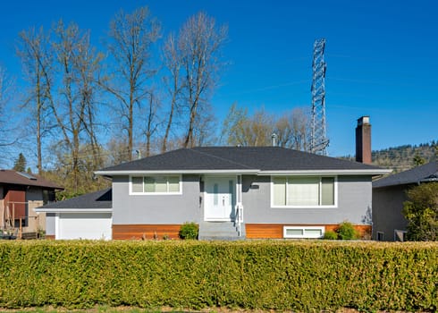 Family house with green fence on the front yard and power line on the back. Residential house on sunny day in British Columbia, Canada