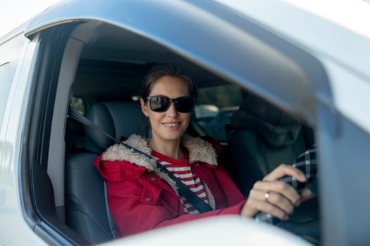 Beautiful woman with sunglasses sit in car and look at camera through window of car also look at camera with smiling in concept of safe drive on the road.