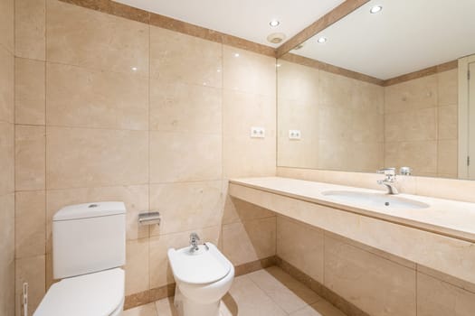 Toilet bidet and long unit with sink and large mirror. Standard filling of bathroom in hotel room offers essential comfort to guests